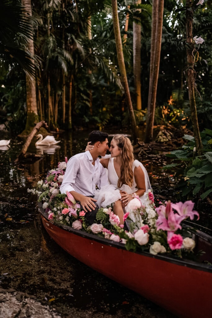 Family Photographer, a man and woman sit on a small row boat in the tropical jungle, it is filled with flowers, they are just married