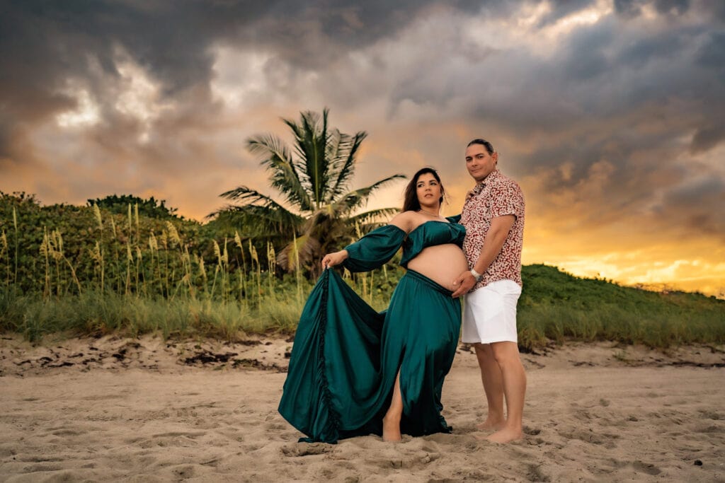 Maternity Photographer, a man and his expectant wife stand on a tropical beach at sunset